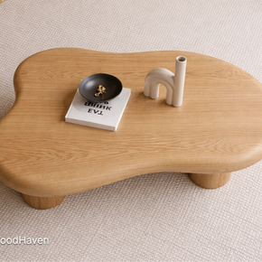 Small oval wooden coffee table with decorative items on a beige carpet, featuring the brand 'Tailor Wood Haven'.